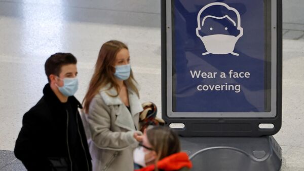 Pedestrians, some wearing face coverings to combat the spread of Covid-19, walk past a sign asking commuters to Wear a face covering, at Liverpool Street train station in central London on December 18, 2021. - Sputnik International